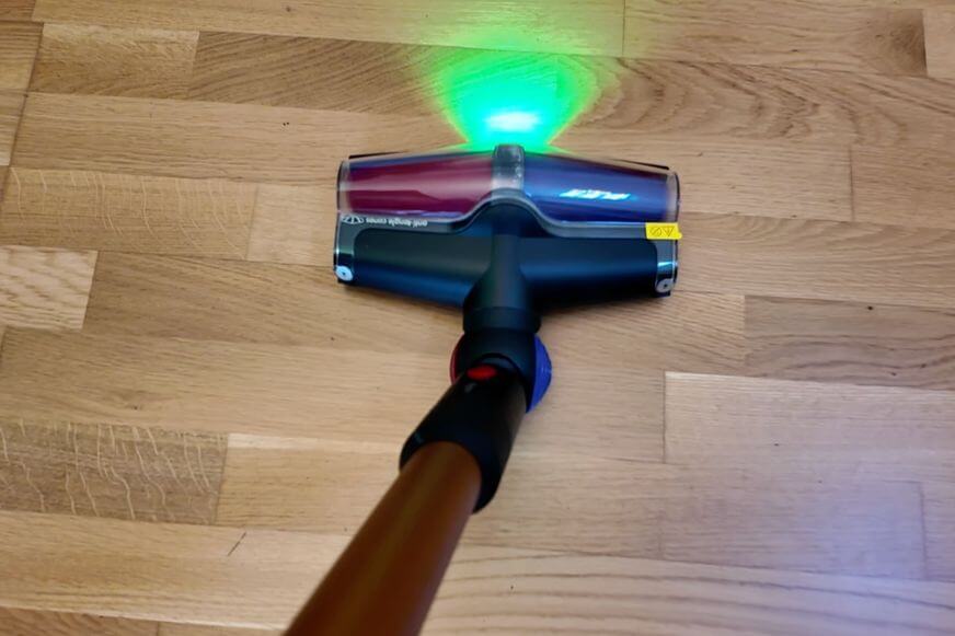 Die neue Bodendüse des Dyson V16 Piston Animal wird im Test gezeigt wie er auf Holzboden saugt und der grüne Laser ist deutlich zu sehen.